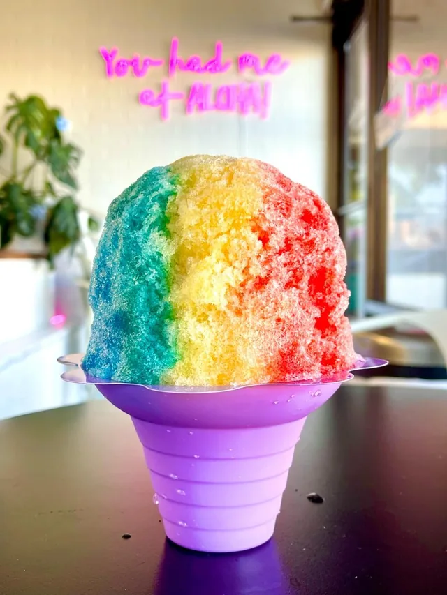 Keiki Rainbow shave ice in a purple flower cup, ALOHA neon behind