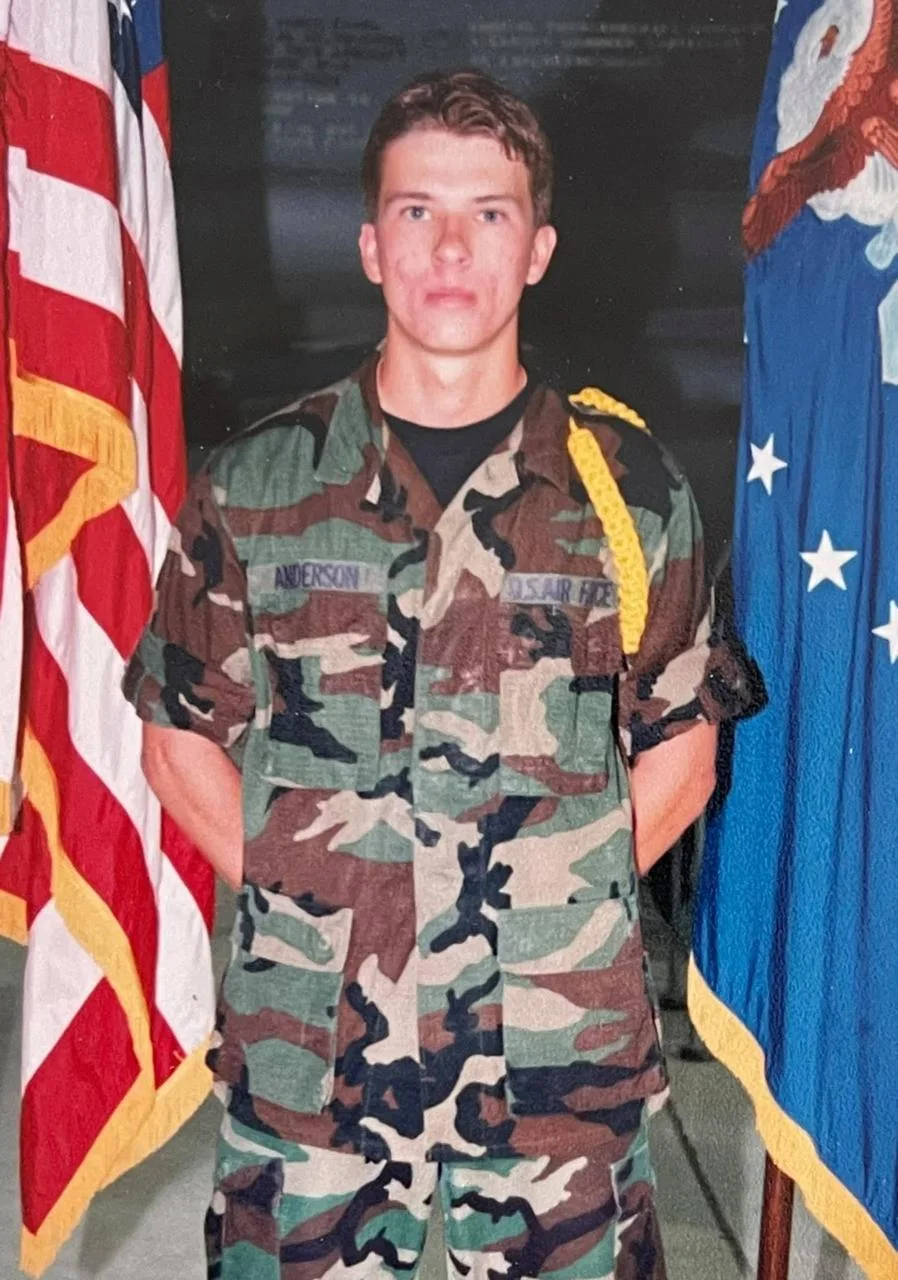 Airman Jimmy Anderson in uniform between the U.S. and Air Force flags